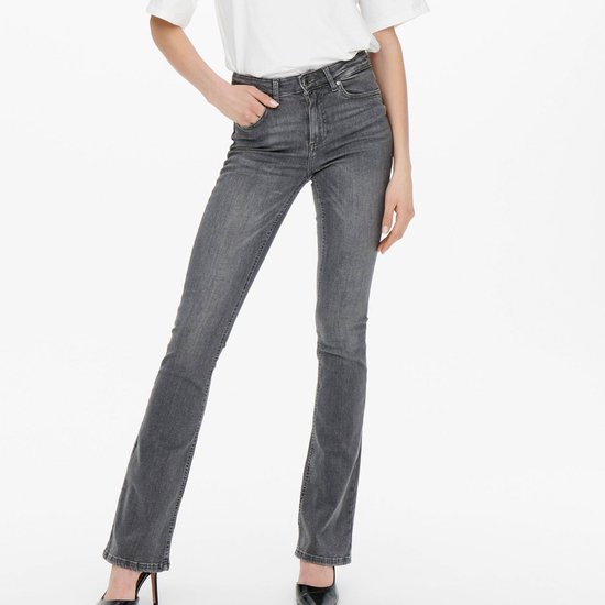 Model in een lichtgrijze flared jeans, met de handen in de zakken.