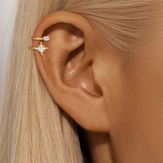 Gouden earcuff met stervormige zirkonia's en een enkele steen, gedragen op een oor.