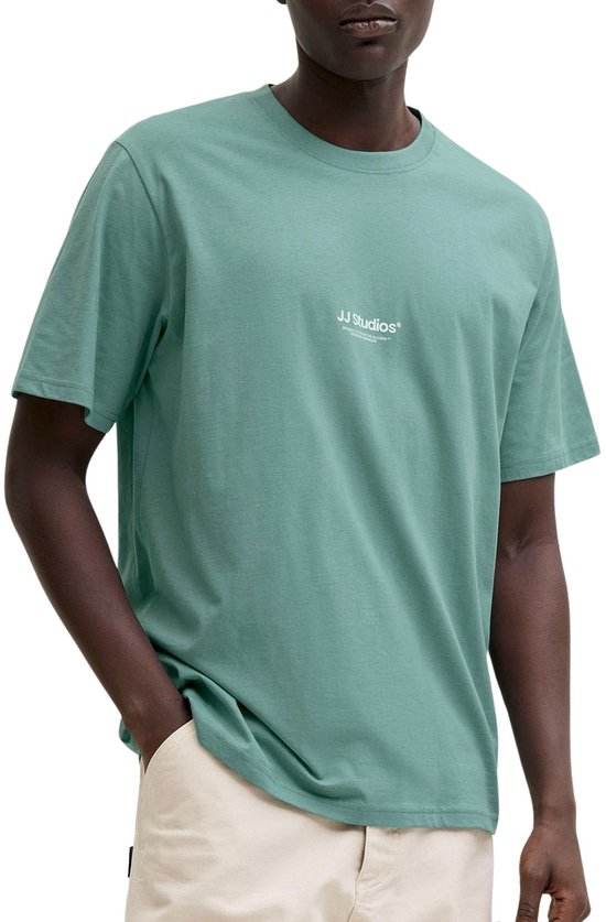 Man draagt jade groen t-shirt met 'JJ Studios' logo, met één hand in de zak.