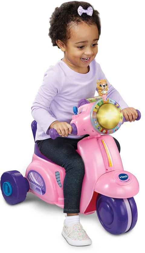 Meisje zit op roze VTech driewieler loopscooter met paarse details en een knipperend lampje.