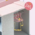 Close-up van een grijs poppencommode met witte stippen, roze matras en drie roze hangers met kleding.
