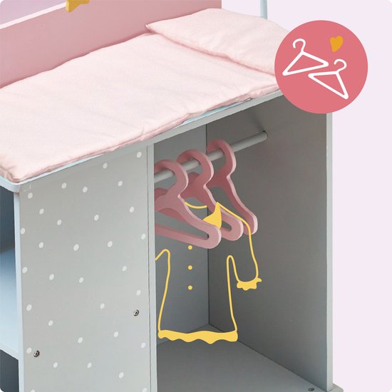 Close-up van een grijs poppencommode met witte stippen, roze matras en drie roze hangers met kleding.