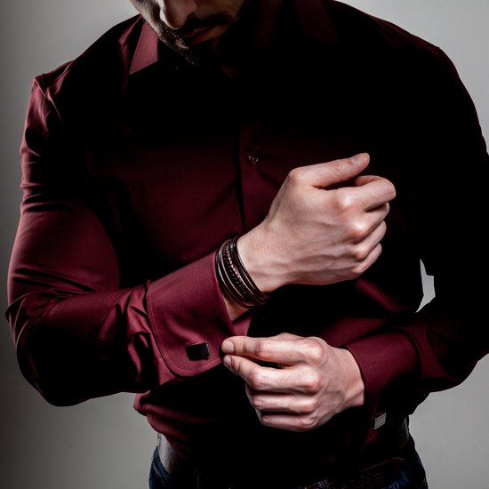 Bruine gevlochten en gladde leren armbanden van SERASAR met donkere sluiting, gedragen door een man met een bordeauxrode satijnen blouse.