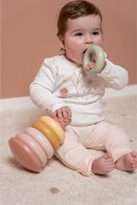 Baby met stapelringenset. De baby houdt een groene ring voor de mond, de roze stapelringenset ligt naast de baby.