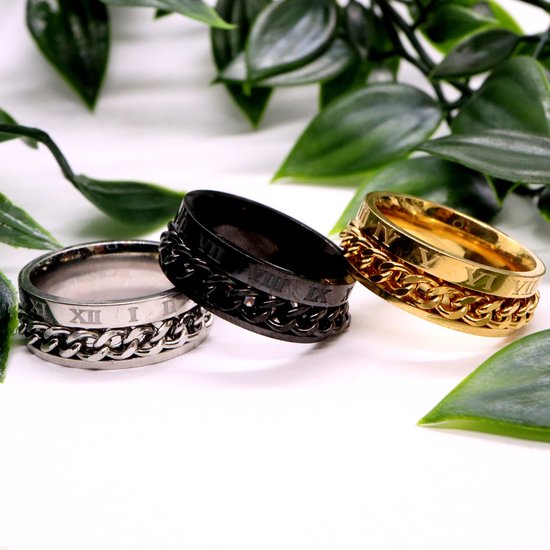 Zilverkleurige, zwarte en gouden ringen met schakelketting en Romeinse cijfers, tussen groene bladeren.