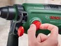 Vinger draait rode instelknop op groene Bosch boorhamer.