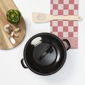 Zwarte braadpan met blauwe rand, deksel erop, naast een groene paprika en knoflook.