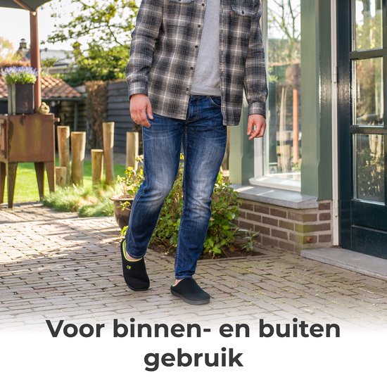 Een man loopt buiten met een geruite blouse, blauwe jeans en zwarte pantoffels.