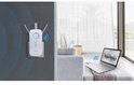 Witte TP-Link wifi-repeater, in een woonkamer, aangesloten op een stopcontact nabij een bank.