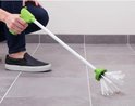 Een persoon vangt een spin met een groene spinnenvanger op een grijze tegelvloer.