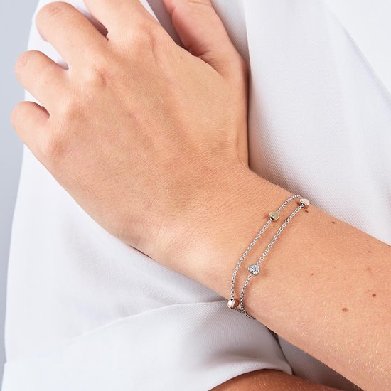 Zilverkleurige armband met twee schakels en kleine hartjes in zilver, rosé- en geelgoud, gedragen door een vrouw met witte blouse.
