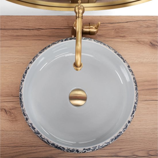 Lavabo blanc à motif floral bleu et blanc et robinet en laiton, vu de dessus.