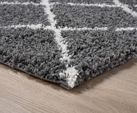 Donkergrijs hoogpolig vloerkleed met wit ruitpatroon.