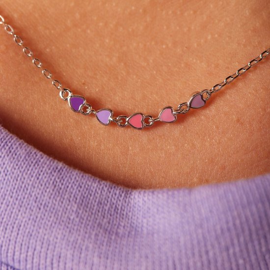 Zilverkleurige ketting met zeven gekleurde emaille hartjes (paars, roze) gedragen door een meisje met paarse trui.