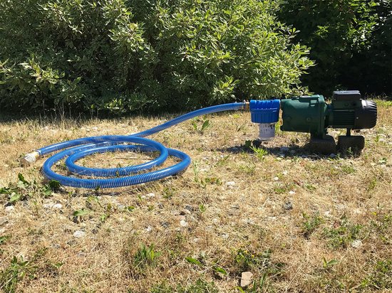 Groene pomp met een blauwe slang die door droog gras loopt.
