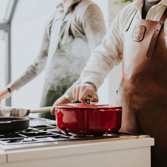 Rode gietijzeren braadpan op een kookplaat, met twee personen in de keuken.