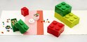 Veelkleurige LEGO-stenen verspreid op een tafelkleed, met rode en groene LEGO-opbergdozen en enkele losse stenen.