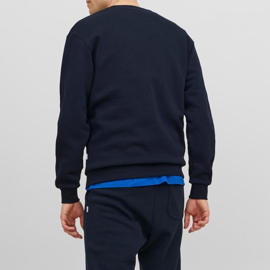 Man met donkerblauwe, effen sweater met ronde hals en blauwe rand van het shirt eronder, gezien van achteren.