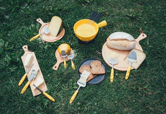 Tafel gedekt met kaas, brood en fondue; diverse kaasschaven met gele handvatten.