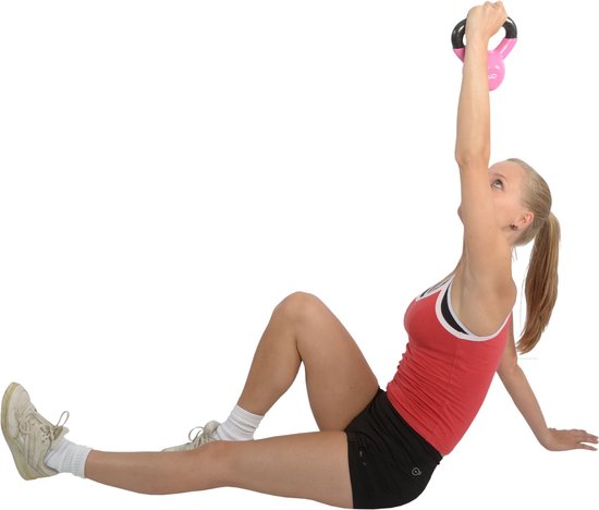 Vrouw met blonde paardenstaart in rode sporttop en zwarte short, houdt roze kettlebell boven haar hoofd.