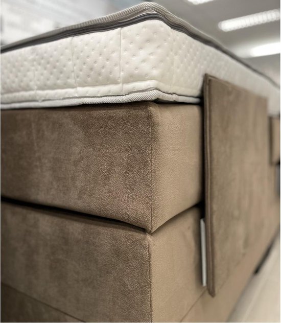 Detail van een wit topdekmatras met ruitstiksels op een bruine boxspring.