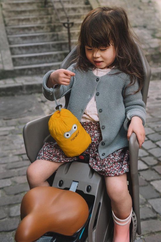 Meisje in kinderzitje met gebreide vest, bloemenrok en een opgevouwen gele regenponcho met oogjes.
