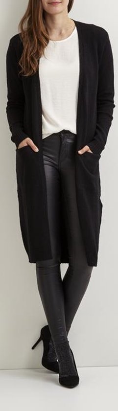 Model draagt een zwarte lange gebreide vest met zakken over een witte top.