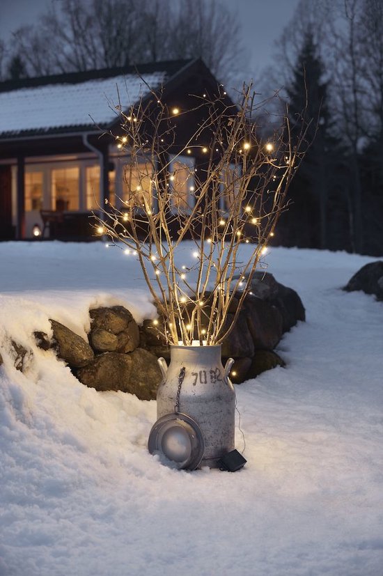 Takken in een metalen melkbus verlicht door warmwitte micro-leds in de sneeuw.