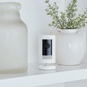 Witte Ring Stick Up Cam op een plank tussen decoratieve vazen.