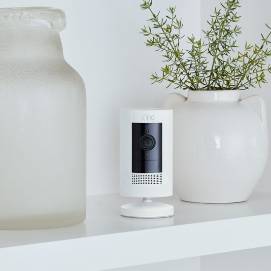 Witte Ring Stick Up Cam op een plank tussen decoratieve vazen.