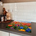 Een kookplaatbeschermer met een kleurrijk bloemenveld van rode, roze en blauwe klaprozen, op een donker aanrecht.