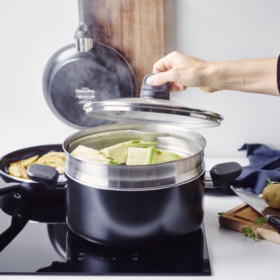 Une cocotte-minute avec des légumes est utilisée sur une plaque de cuisson. Une main soulève le couvercle.
