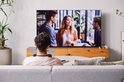 Man van achteren gezien, draagt een nekband speaker en kijkt tv. Blauwe geluidsgolven om zijn hoofd.