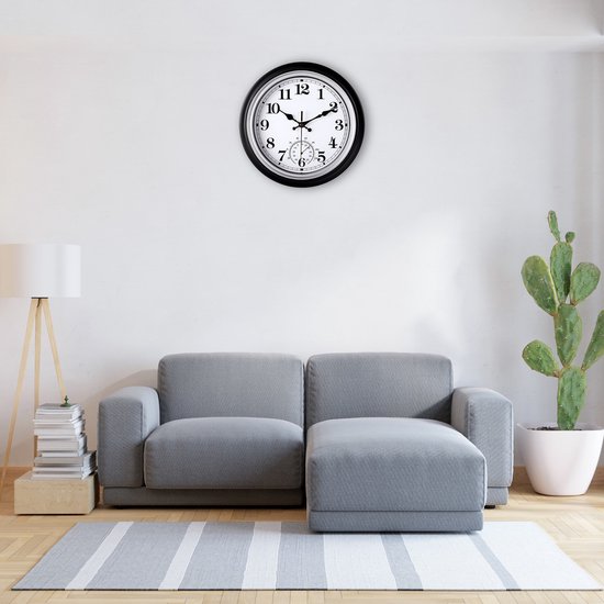 Zwarte wandklok met witte wijzerplaat en thermometer, 30 cm, boven een grijze bank