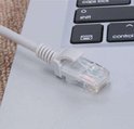 Transparante RJ45-connector van een grijze ethernetkabel, op een laptop toetsenbord.