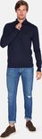 Man in donkerblauwe trui met rits tot de borst en jeans, staand.