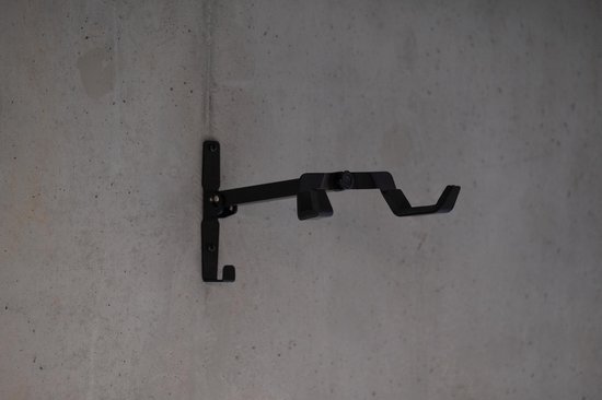 Zwarte, metalen fietsmuurbeugel met twee beschermde haken, bevestigd aan een betonnen muur.