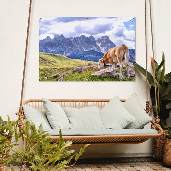 Een bruine koe in de Alpen op een poster boven een bank.