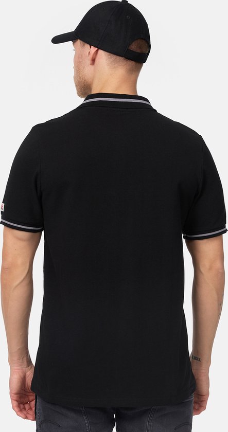 Achterkant van een model dat een zwarte Lonsdale polo draagt. Polo heeft dubbele grijze en witte strepen op de mouwen.