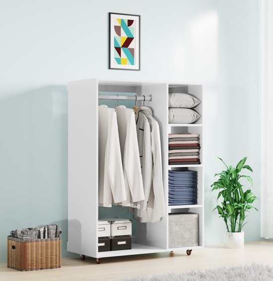 Witte kledingkast met hanggedeelte en legplanken, gevuld met kleding, kussens en kasten. Wielen aan de onderkant, plant op de achtergrond.