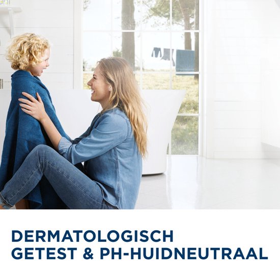 Moeder met spijkerblouse en kind met krullen in blauwe handdoek, lachend in een lichte badkamer. Tekst: Dermatologisch getest & pH-huidneutraal.