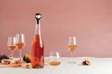 Een fles rosé met een vampier-wijnstopper, omringd door glazen en fruit op een tafel.
