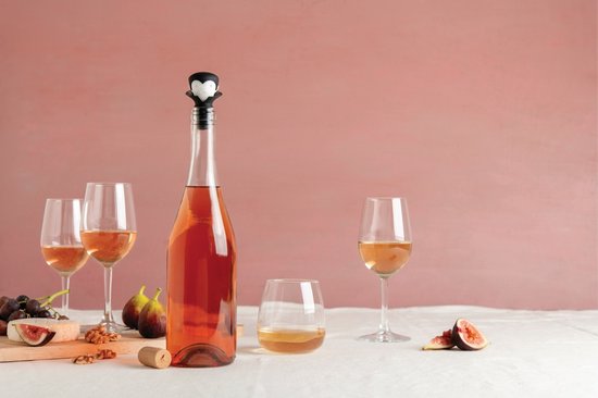 Een fles rosé met een vampier-wijnstopper, omringd door glazen en fruit op een tafel.