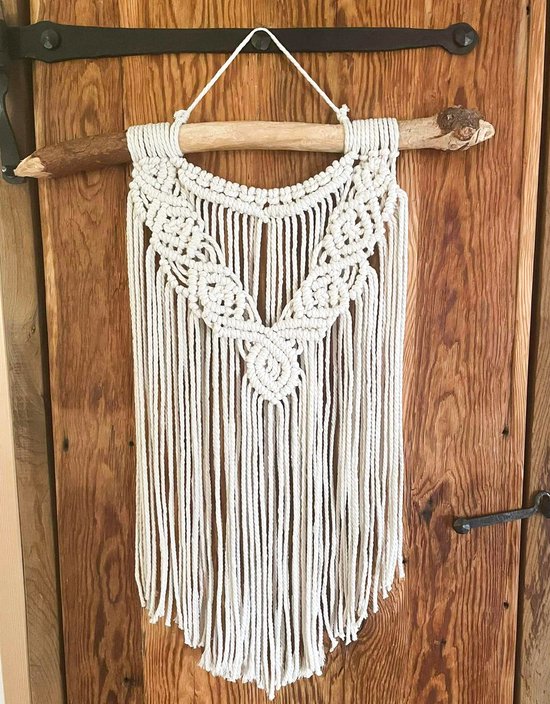 Macramé wandkleed in natuurlijke tint met gedetailleerd patroon, hangend aan een boomtak.