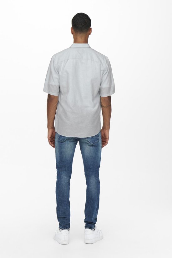 Achterkant van een lichtgrijs kortgerokt overhemd over een jeans.