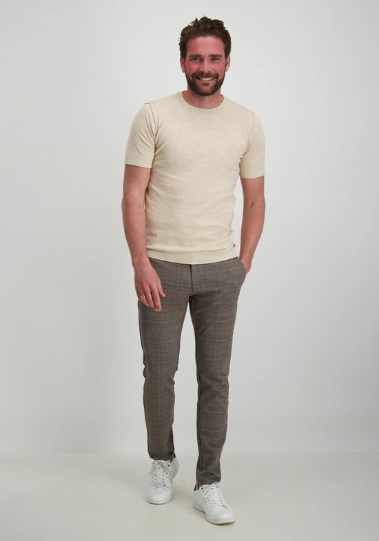 Homme barbu, souriant, portant un t-shirt beige et un pantalon à carreaux.