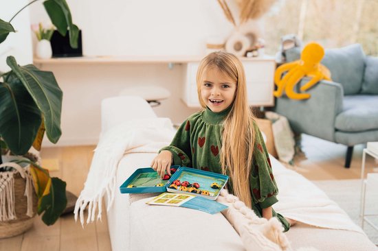Une fille joue avec le jeu LogiBugs sur un canapé, tenant la boîte de jeu ouverte.