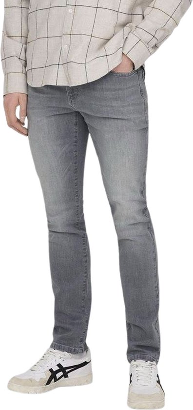 Model in een grijze slim fit spijkerbroek en een geblokt overhemd, staand.