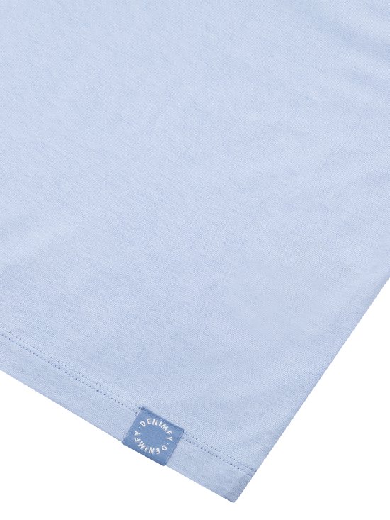 Detail van een effen lichtblauwe top met een klein blauw logo-label.