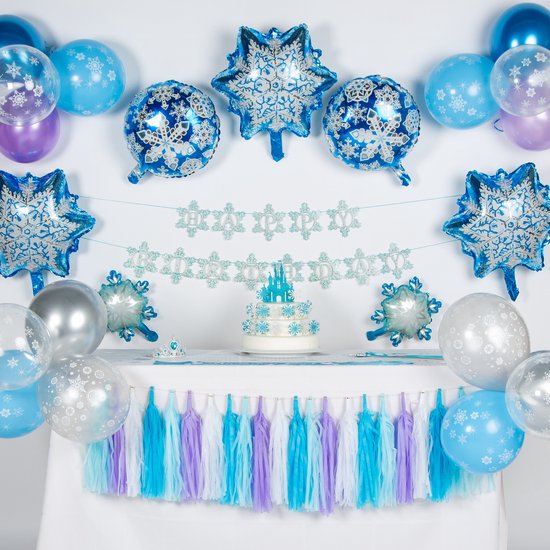 Een feesttafel versierd met Frozen thema: taart met kasteel, blauwe en witte ballonnen, sneeuwvlok slinger, en kwastjes slinger.
